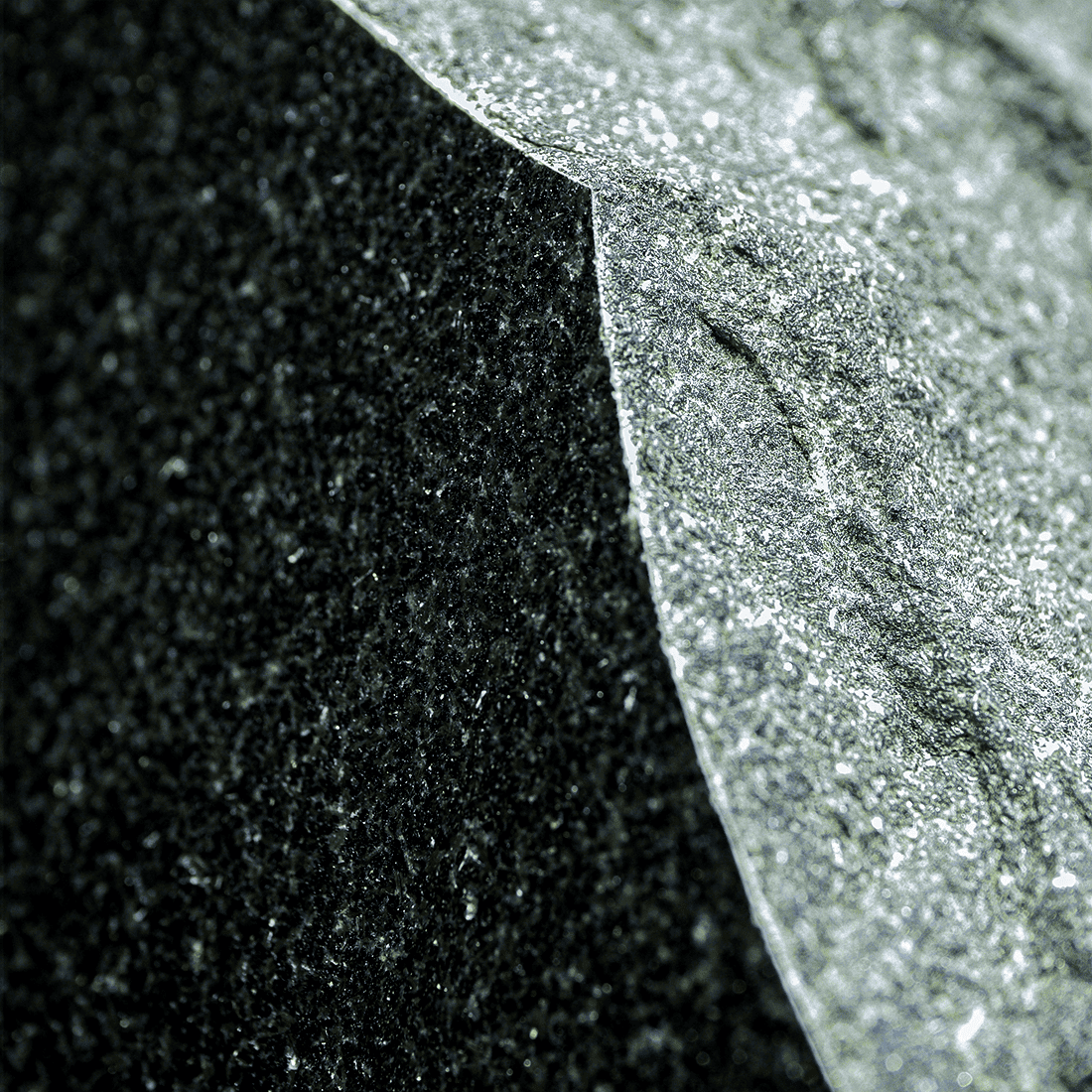 Close-up of polished black granite memorial stone edge with rough natural finish