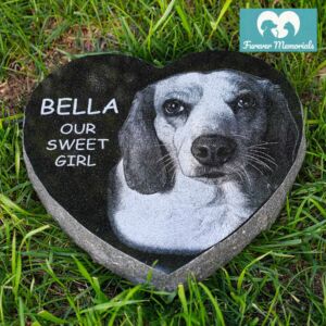 Heart-shaped black granite pet memorial engraved with a portrait of Bella the dog and the inscription “Bella – Our Sweet Girl,” placed in green grass.