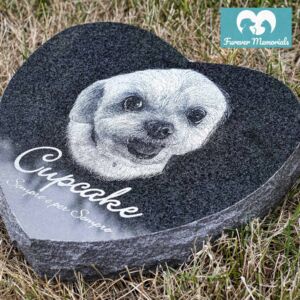 Heart-shaped black granite pet memorial engraved with a portrait of Cupcake the dog and the inscription “Cupcake – Siempre en mi Siempre,” placed on grass.