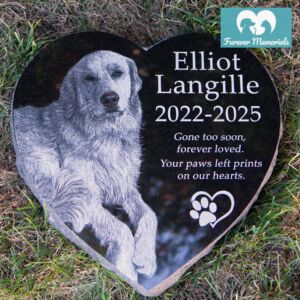 Heart-shaped black granite pet memorial for Elliot Langille (2022–2025) engraved with a detailed portrait of a long-haired dog, placed naturally in grass as a garden grave marker.