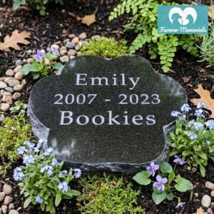 Black granite paw-shaped pet memorial engraved with the name Emily (Bookies) and the dates 2007–2023, placed in a peaceful garden bed surrounded by small blue and purple flowers.