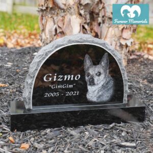 Black granite upright pet memorial engraved with a portrait of Gizmo the dog, including the nickname “GimGim” and the dates 2005–2021, displayed in a garden setting.