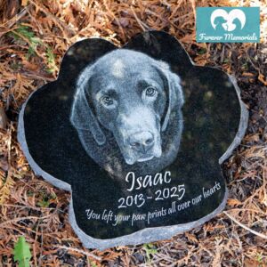 Custom engraved black granite paw-shaped pet memorial for dog Isaac with detailed portrait engraving and inscription, placed in an outdoor garden setting