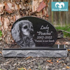 Black granite oval pet memorial headstone engraved with a portrait of Lady “Picachu” the dog, including the dates 2007–2022 and the inscription “Forever in our hearts,” placed in a garden setting.
