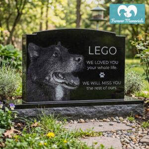 Black granite pet memorial headstone engraved with a detailed portrait of Lego the dog and the inscription “We loved you your whole life, we will miss you the rest of ours”, placed in a peaceful backyard garden setting.