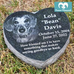 Black granite heart-shaped pet memorial stone engraved with a portrait of Lola “Bean” Davis the dog, including the dates October 15, 2004 – June 27, 2022 and a memorial quote, placed in grass in a garden setting.