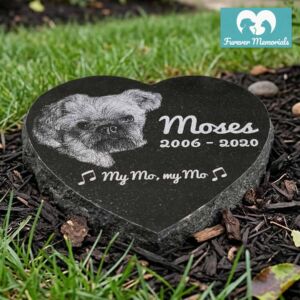 Heart-shaped black granite pet memorial engraved with a portrait of Moses the dog, including the inscription “My Mo, my Mo” with musical notes and the dates 2006–2020, placed in a garden bed.