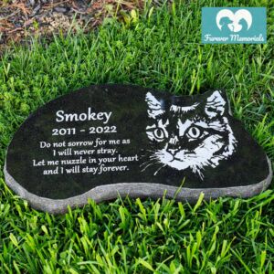Black granite cat memorial stone engraved with a portrait of a cat named Smokey and the dates 2011–2022, placed in grass in an outdoor garden setting.