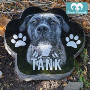Custom engraved black granite paw-shaped pet memorial for dog Tank featuring detailed portrait engraving and paw prints, displayed in a garden setting
