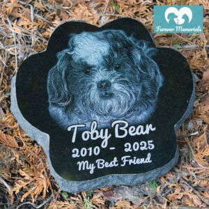 Custom engraved black granite paw-shaped pet memorial for dog Toby Bear with detailed portrait engraving and inscription “My Best Friend,” displayed in a garden setting