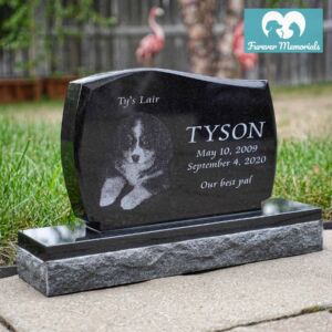 Black granite upright pet memorial engraved with a portrait of Tyson the Bernese Mountain Dog puppy and the inscription “Ty’s Lair,” with Tyson’s name and memorial dates, displayed in a backyard garden setting.